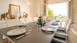 A dining table set for four with white chairs, a vase with purple flowers, and a bottle of wine.