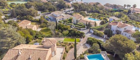 An aerial view of a coastal residential area with houses, a swimming pool, and a view of the sea.