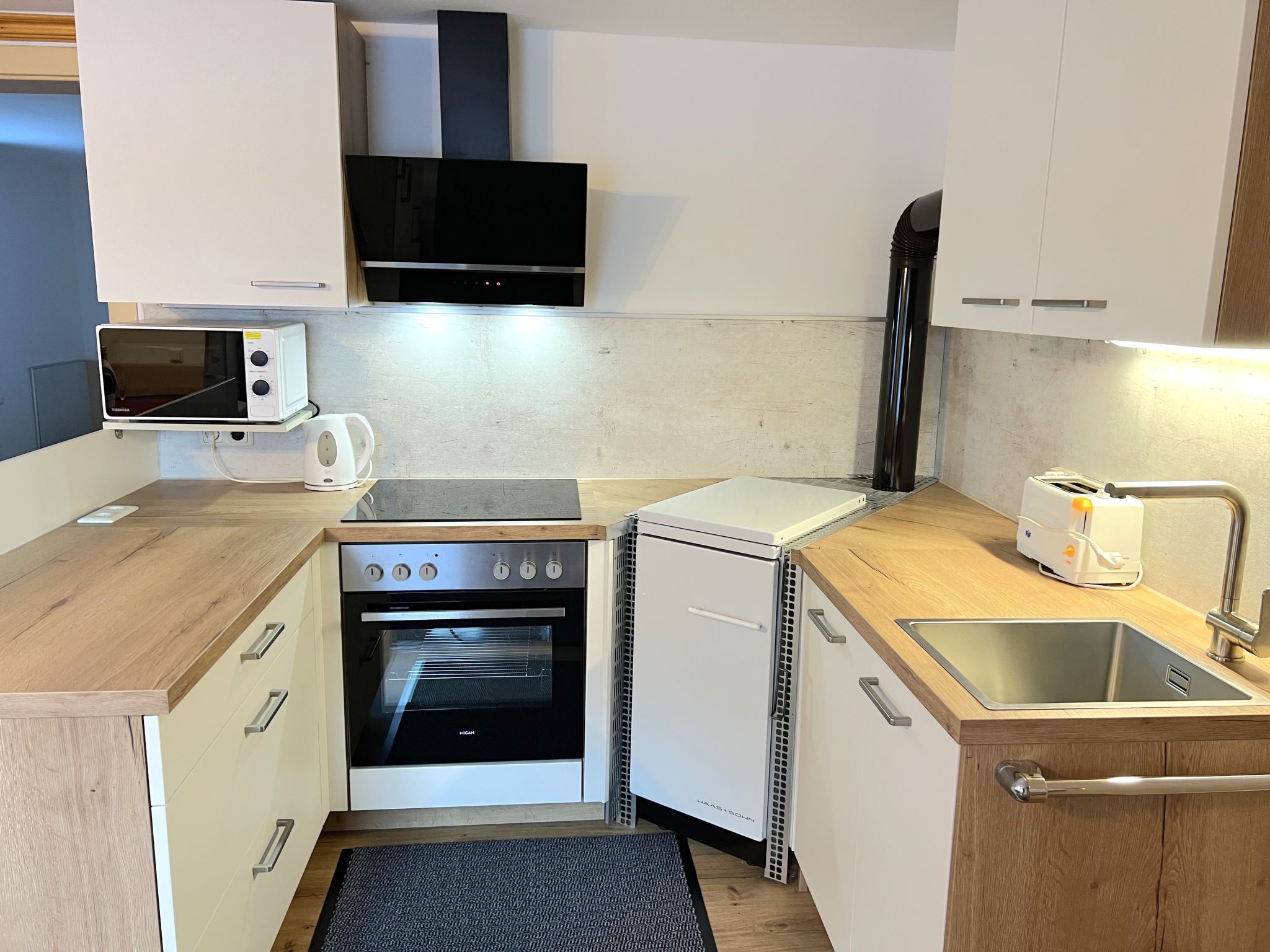 Uma cozinha compacta com micro-ondas, torradeira, forno e pia.