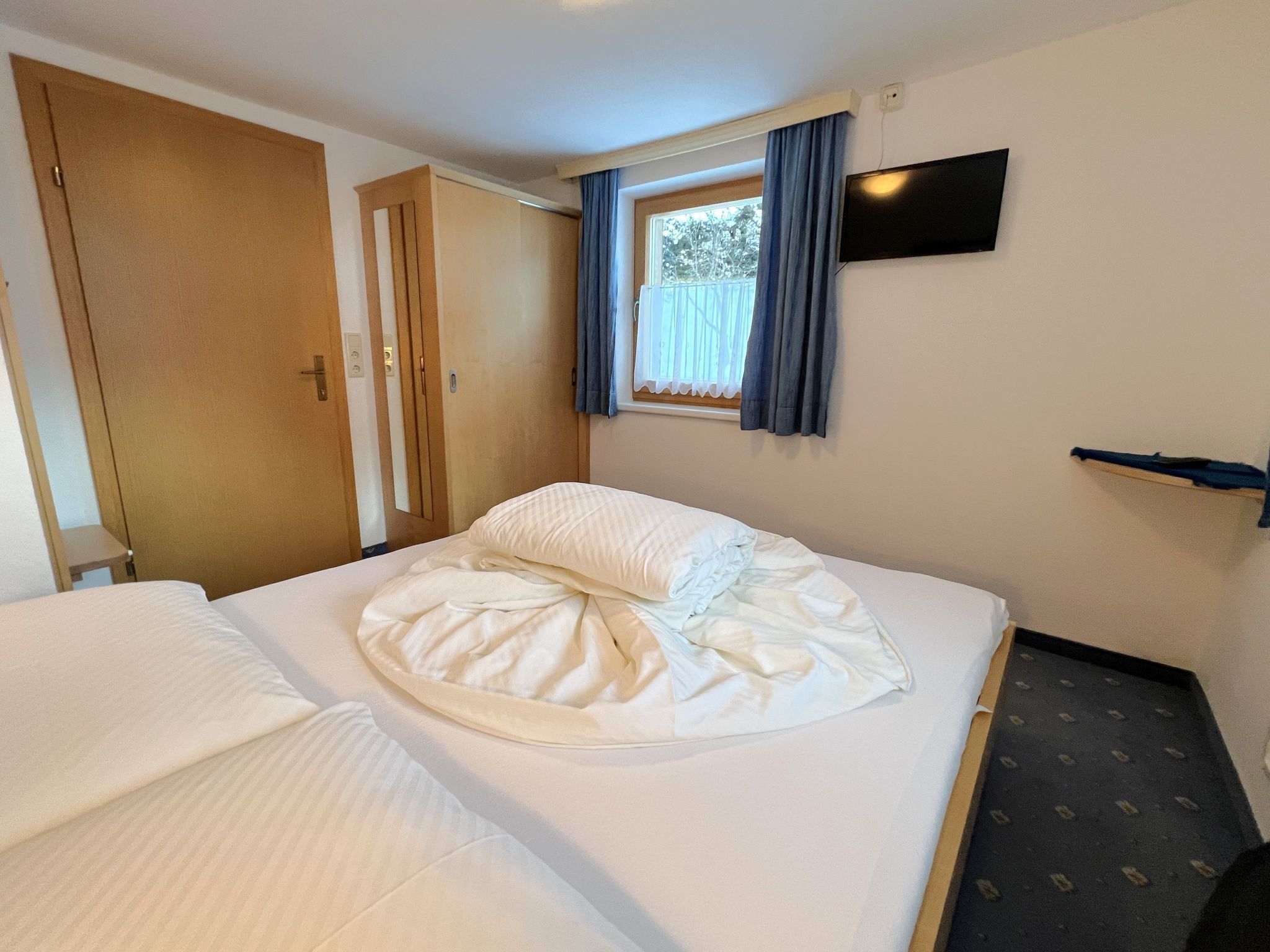 A hotel room with a bed, a TV mounted on the wall, and a window with curtains.