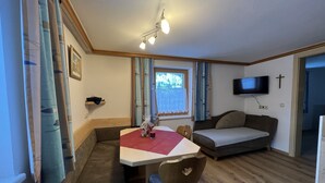 Una sala de estar acogedora con una mesa de comedor, un sofá y un televisor montado en la pared.