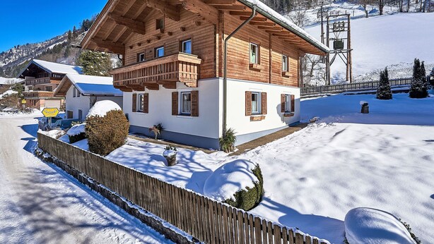 Una cabaña de madera con balcón, rodeada de terreno y árboles cubiertos de nieve.