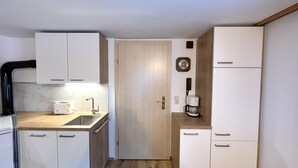 Una cocina compacta con gabinetes blancos, un lavamanos, una cafetera y un reloj en la pared.