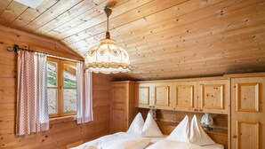 Une chambre dans une cabane en bois, avec un lit, des rideaux et un luminaire suspendu.