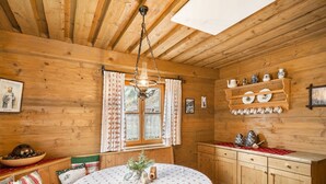 L’intérieur d’un chalet en bois chaleureux, avec une table à manger ronde, des meubles en bois et une fenêtre agrémentée de rideaux.
