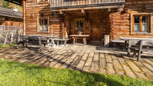 Un bâtiment rustique en bois, doté d’un balcon, d’un espace extérieur aménagé pour s’asseoir et d’une terrasse dallée.