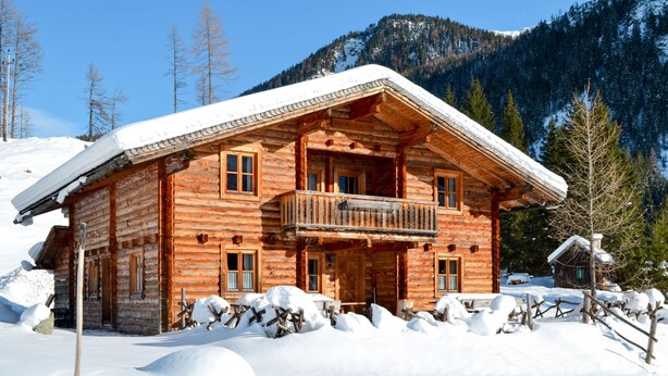 Une cabane en rondins dotée d’un balcon, entourée de neige et de montagnes.