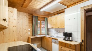 Une cuisine rustique aménagée dans une cabane en bois, avec un poêle encastré, des placards en bois et une fenêtre agrémentée de rideaux.