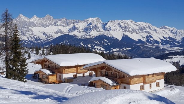 A wooden chalet with a snow-covered roof, set against a backdrop of snow-capped mountains under a clear blue sky. - Vacation home Aualm by Interhome (Forstau)