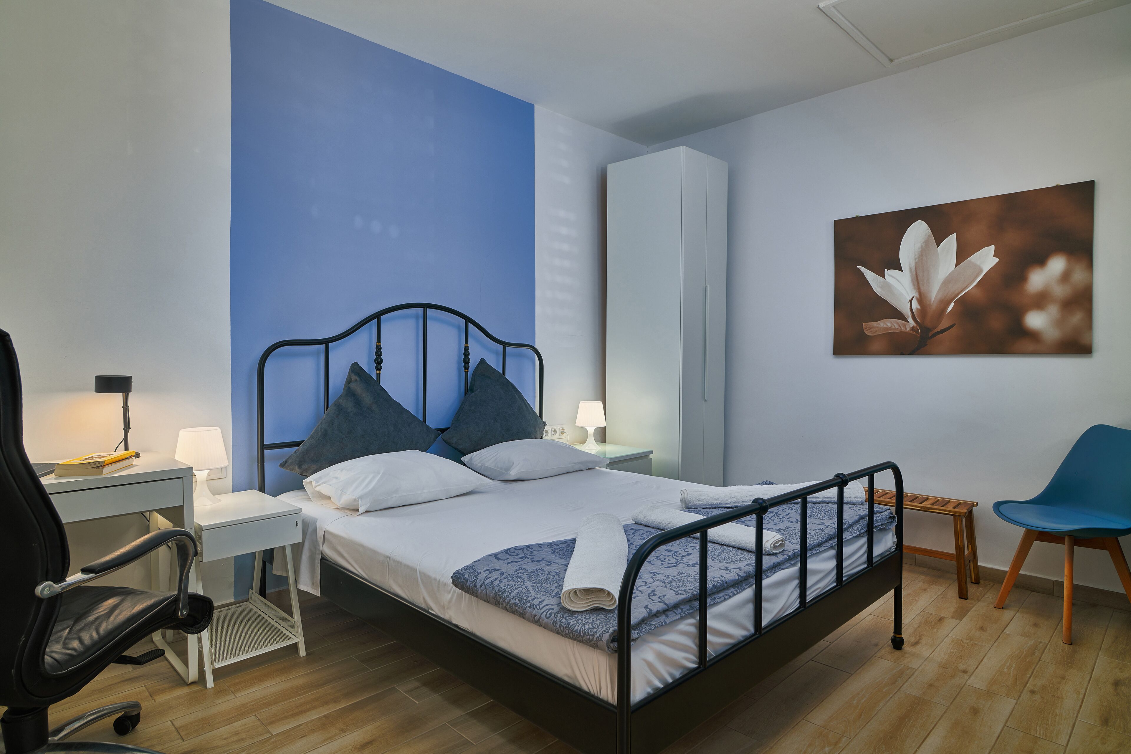 Ein ordentlich eingerichtetes Schlafzimmer mit Bett, Schreibtisch, Stuhl und einem an der Wand befestigten Kleiderschrank.