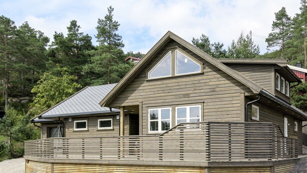 Une maison en bois à deux étages, dotée d’un toit en pente, de grandes fenêtres et d’une terrasse en bois.