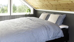 Une chambre avec un plafond en pente, une grande fenêtre et un lit recouvert d’une couette à carreaux.
