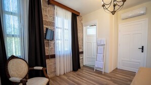 A room with a wooden floor, a chair, a TV, a chandelier, and a door. - Cunda Mahmut Bey Konağı (Ayvalik)