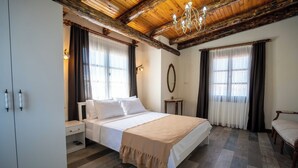 A bedroom with a large bed, wooden ceiling beams, a chandelier, and a wardrobe. - Cunda Mahmut Bey Konağı (Ayvalik)
