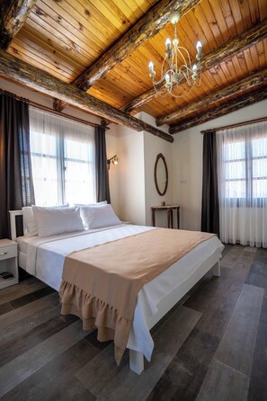 A bedroom with a wooden ceiling, a bed with white bedding, a bedside table, and a mirror on the wall. - Cunda Mahmut Bey Konağı (Ayvalik)