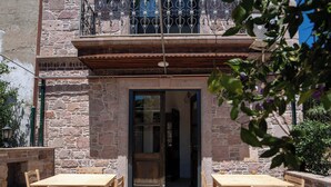 An outdoor patio with wooden tables and chairs, a stone wall, and a balcony with a metal railing. - Cunda Mahmut Bey Konağı (Ayvalik)
