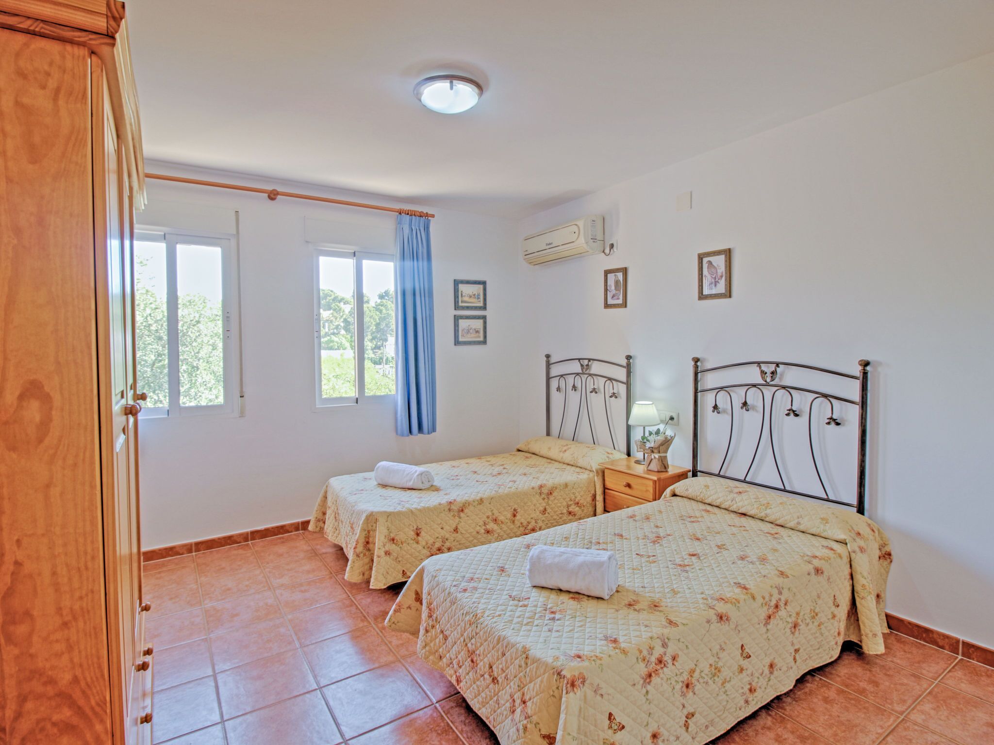 Una camera da letto con due letti, un armadio in legno, una finestra con tende e una lampada a soffitto.