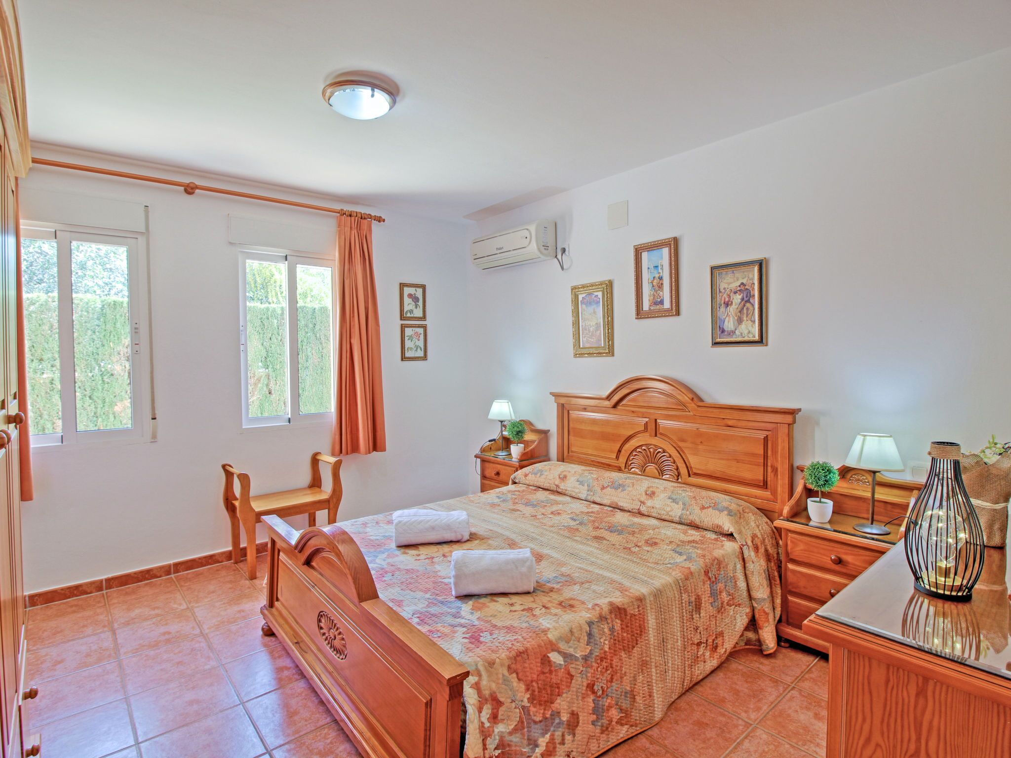 A bedroom with a wooden bed, a wooden chair, a nightstand, a lamp, and a small table with a plant.
