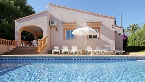 A poolside area with a clear blue pool, white lounge chairs, and a building with a tiled roof and a staircase leading to an entrance. - Dulce Vida by Interhome (Calpe/Calp)