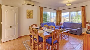 A dining area with a table set for four, surrounded by wooden chairs with blue cushions. There is a sofa and a small table with a lamp in the living area. - Dulce Vida by Interhome (Calpe/Calp)