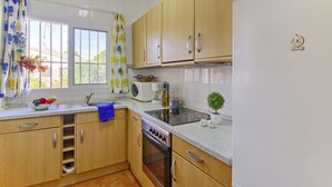 A kitchen with wooden cabinets, a stove, a sink, and a window with curtains. - Dulce Vida by Interhome (Calpe/Calp)