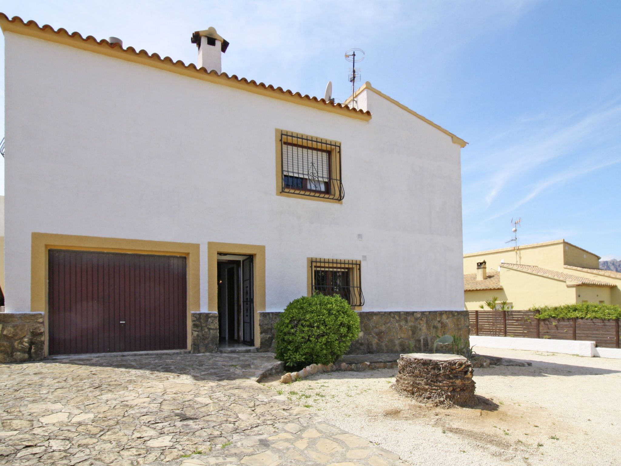 A two-story building with a white facade, a stone-paved entrance, and a small bush in the front yard.