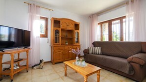Ein Wohnzimmer mit Fernseher auf einem Holzständer, einem braunen Sofa, einem Holzschrank und einem Fliesenboden.