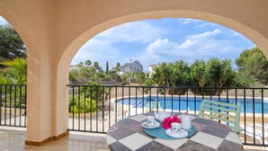 Ein Balkon mit Blick auf einen Swimmingpool, ein Tisch mit kariertem Tischtuch und ein Stuhl.