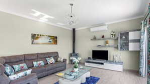 Una sala de estar moderna con un sofá gris, una mesa de centro de vidrio, un televisor de pantalla plana y objetos decorativos en estantes.