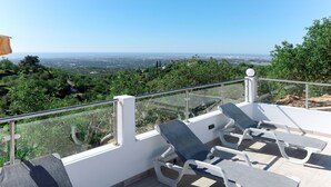 Una terraza con sillones blancos y barandilla de cristal que ofrece vistas panorámicas del paisaje.