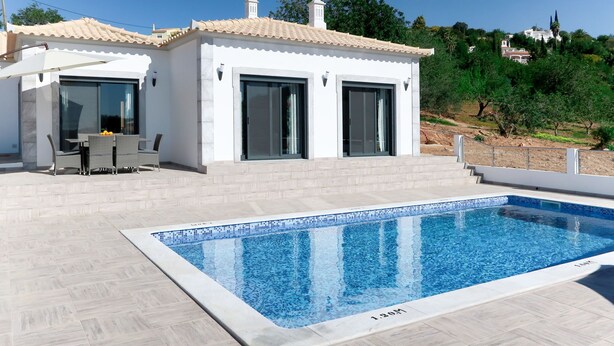 Una casa moderna con piscina, un patio con mobiliario exterior y vistas del paisaje circundante.