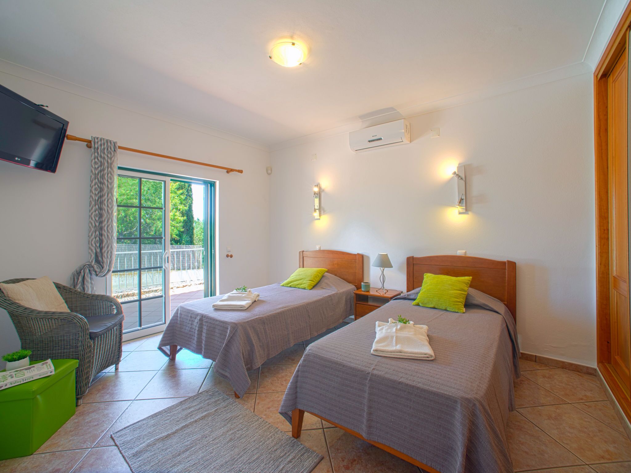 Una habitación de hotel con dos camas, televisión, balcón y una silla verde.