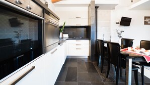 Une cuisine moderne avec des meubles blancs, un four en acier inoxydable et un coin repas avec des chaises et une table noires.