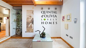 Un intérieur moderne avec une table en verre, une photographie d’époque et un mur orné de l’inscription « QUINTAL d’OLÍVIA LOVELY HOMES ».