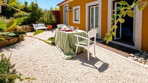 Une terrasse avec une table dressée pour deux personnes, entourée de gravier, avec un bâtiment jaune et de la verdure en arrière-plan.