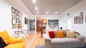 Un salon moderne avec un canapé beige et un fauteuil jaune, une cuisine en arrière-plan et un coin repas avec une table et des chaises.
