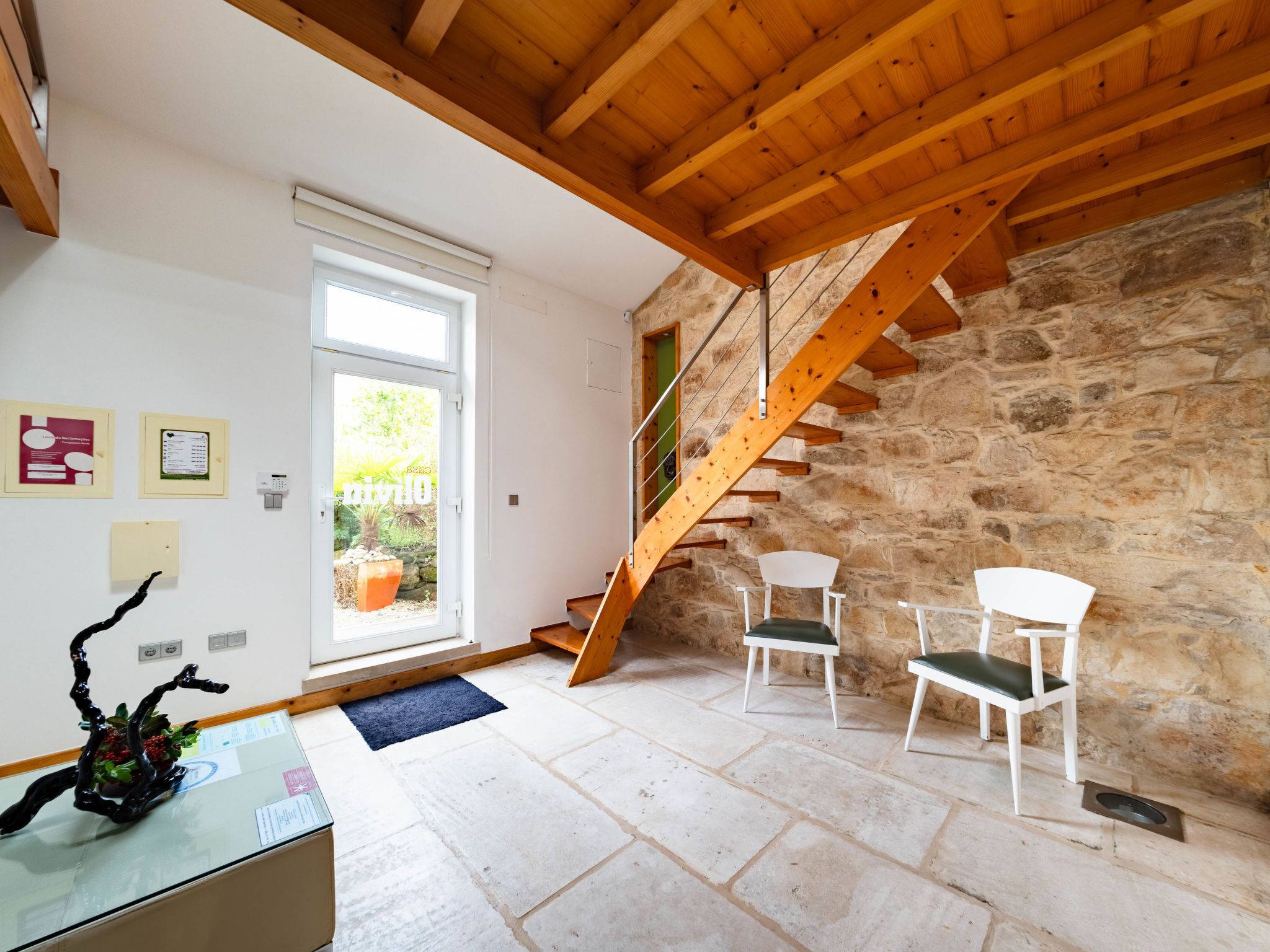 A room with a stone wall, wooden staircase, and white chairs.