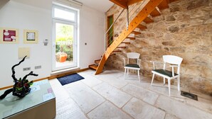 Une pièce avec un mur en pierre, un escalier en bois et des chaises blanches.
