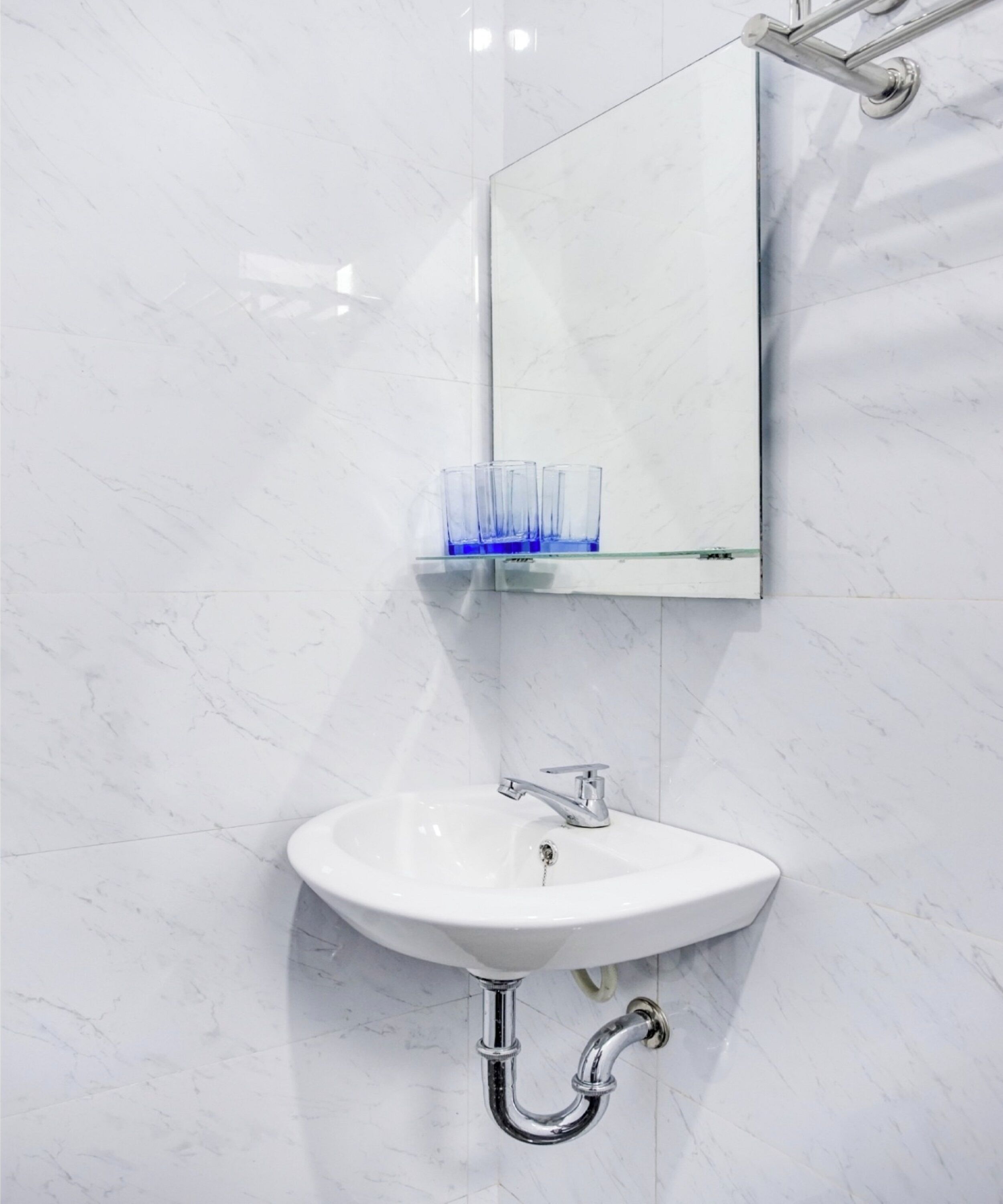 Ein Badezimmer mit einem weißen Marmorwaschbecken, einem Chrom-Wasserhahn und einem Spiegel darüber.