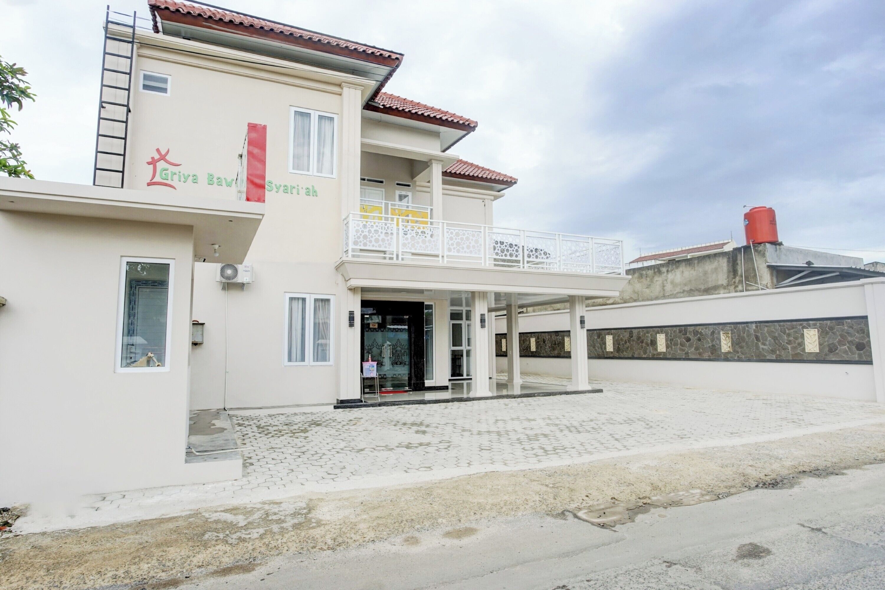 A two-story building with a balcony, a sign reading "Griva Bawol Syarifah," and a red water tank on the roof.