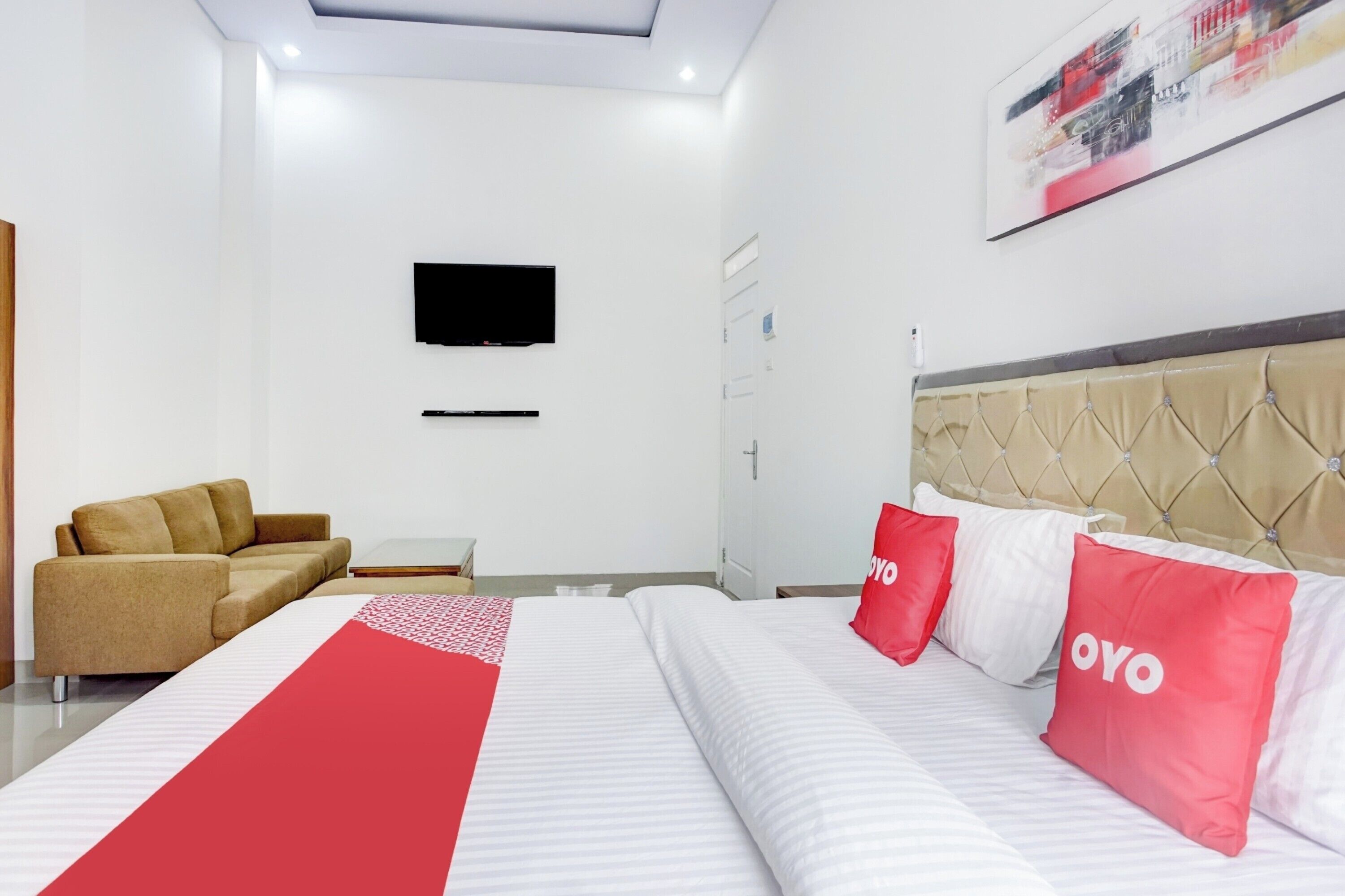 Habitación de hotel con cama, sofá, televisor montado en la pared y un cuadro sobre la cama.