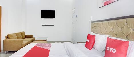 Habitación de hotel con cama, sofá, televisor montado en la pared y un cuadro sobre la cama.