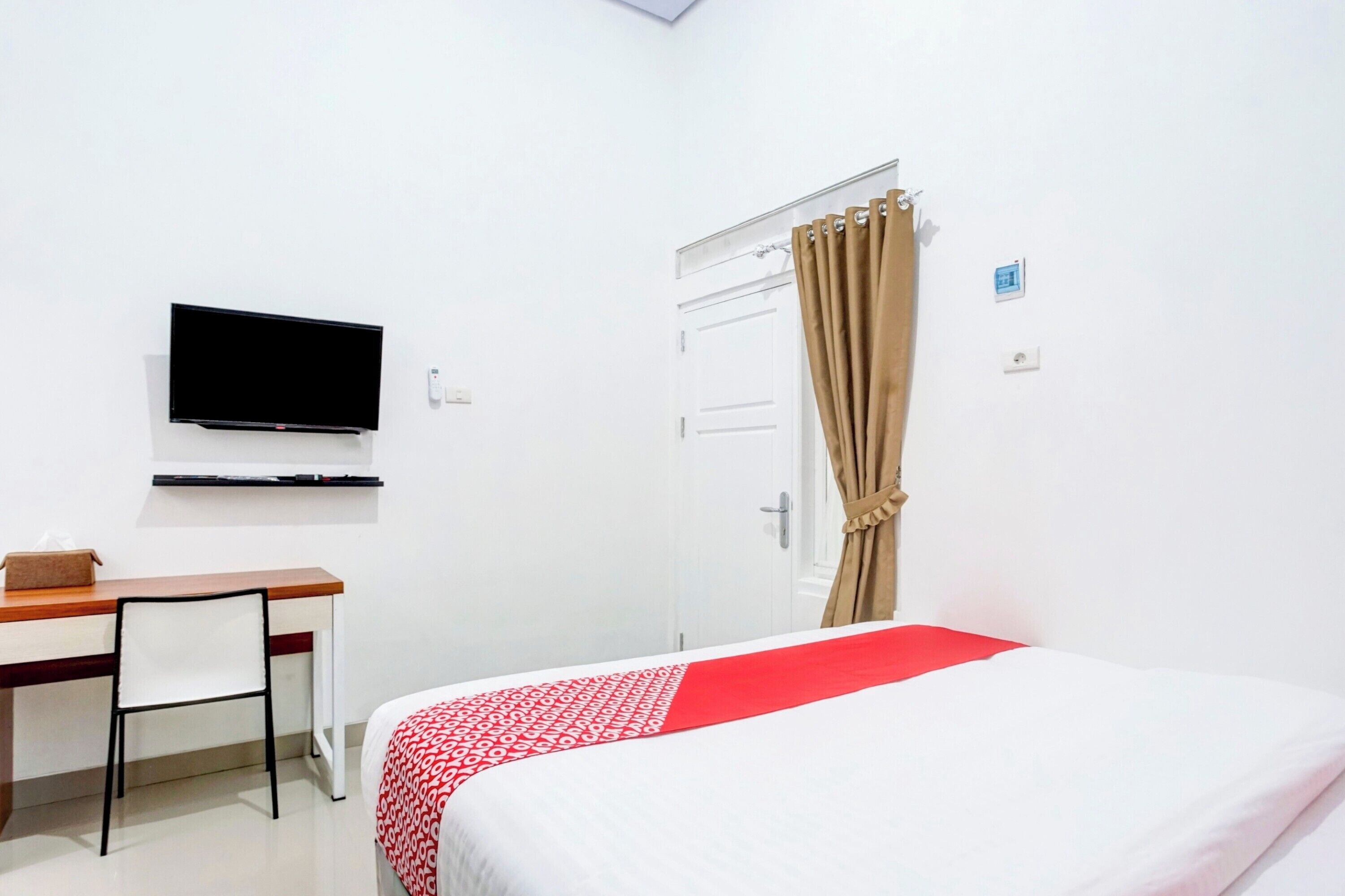 A hotel room with a bed, a desk, a chair, a television, and a door with curtains.