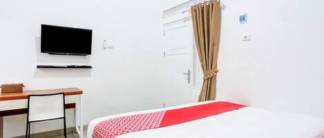 A hotel room with a bed, a desk, a chair, a television, and a door with curtains.