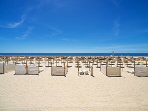 En strand med rader av solstolar och parasoller, en livboj och en klarblå himmel.
