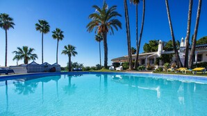 A clear blue swimming pool surrounded by palm trees and lounge chairs.