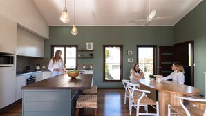 A modern kitchen with a central island, white bar stools, and a dining area with a wooden table and chairs.