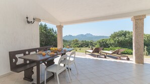 A covered outdoor dining area with a table, chairs, and a view of mountains.