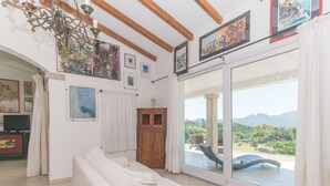 A spacious living room with a white sofa, a wooden cabinet, and a large window offering a view of a balcony with a chair.