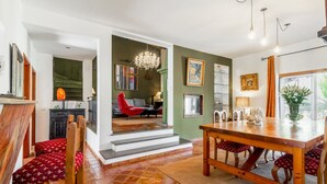 A spacious dining area with a wooden table and chairs, a chandelier, and a view of the living room.